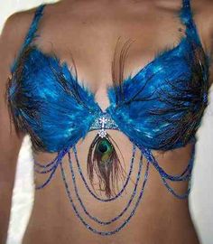 a woman wearing a blue feather bra with chains around her waist and peacock feathers attached to the bra