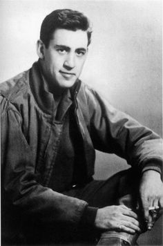 black and white photograph of a man sitting on the floor with his legs crossed, wearing a jacket and tie