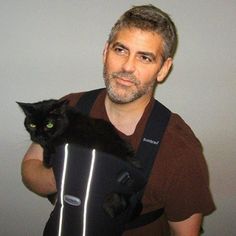 a man is holding a black cat in his back pack while wearing a brown shirt