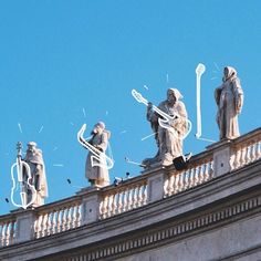 four statues on top of a building with blue sky in the backgrounnd