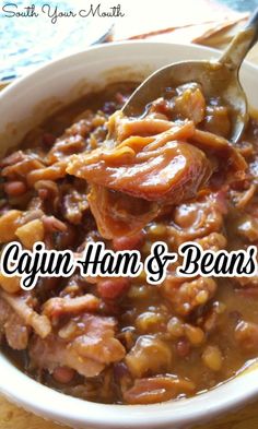 a bowl filled with meat and beans on top of a wooden table next to a spoon