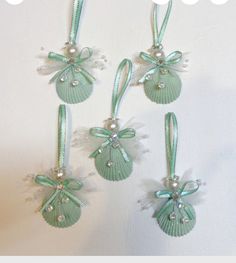 three seashell ornaments are hanging on the wall with pearls and ribbons around them,