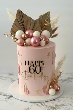 a pink and gold birthday cake with feathers on top