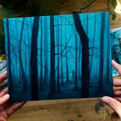 a person holding up a piece of art that looks like a forest with blue trees