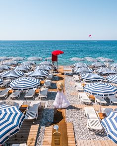 there is a woman sitting on the beach looking out at the ocean and umbrellas