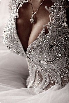 the back of a woman's dress is covered in pearls and beads, while she sits on a bed