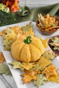 a white plate topped with a pumpkin and fall leaves next to other dishes filled with food