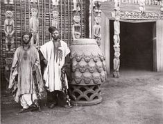 two men standing next to each other in front of an elaborately decorated vase and statue