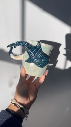 a hand holding a blue and white vase with a fish on it's side