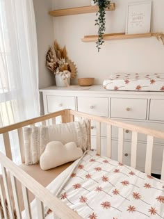 a baby crib in a nursery with white dressers and wooden shelves on the wall