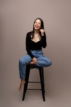 a woman sitting on top of a stool laughing and holding her hand up to her face