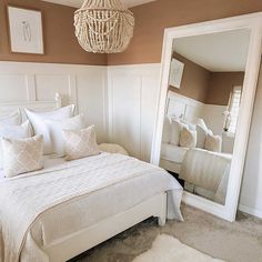 a white bed sitting next to a large mirror in a bedroom under a chandelier