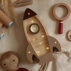 a wooden toy rocket ship next to other toys on a white tablecloth with string lights