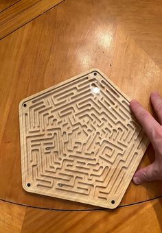 a hand is pointing at a maze board on a table that has been carved into it