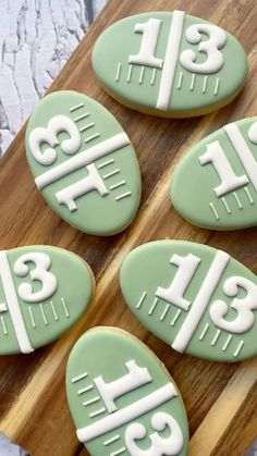 four decorated cookies sitting on top of a wooden cutting board with numbers and letters painted on them