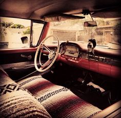 the interior of an old car with a dog sitting in the driver's seat