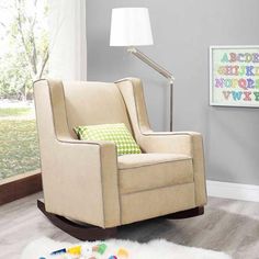 a beige rocking chair with green pillows and a white lamp on the floor in front of a gray wall