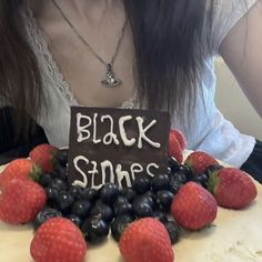 a woman sitting in front of a cake with strawberries and blueberries on it