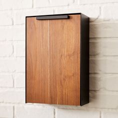 a wooden box mounted to the side of a white brick wall with a black metal frame