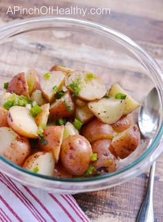 a glass bowl filled with potatoes on top of a wooden table next to a spoon