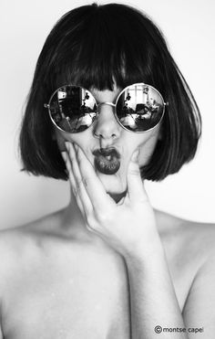 a shirtless woman wearing sunglasses and holding her hands to her face while posing for the camera