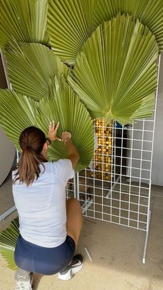 a woman sitting on the ground working on a large palm tree sculpture in front of a fence