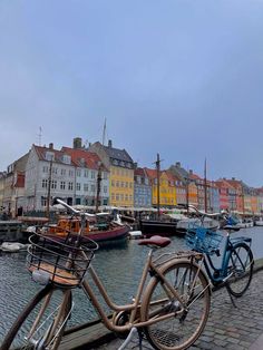 two bicycles parked next to each other on the side of a body of water with buildings in the background