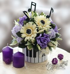 purple and white flowers in a black and white striped vase next to two candles on a table