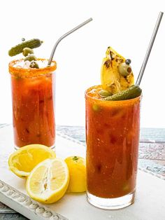 two glasses filled with drinks sitting on top of a table next to lemon wedges