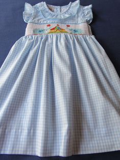 a blue and white gingham dress with an embroidered bird on the chestline