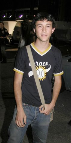 a young man standing in front of a car holding onto a brown belted bag