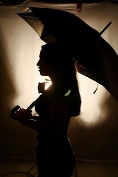 a woman holding an umbrella while standing in front of a white wall with light coming through it