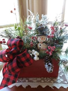 a christmas centerpiece with a snowman and pine cone on the table in front of a window