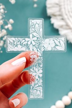 a person holding up a clear cross shaped object with flowers and leaves on the side