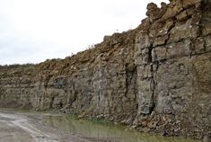 a dirt road next to a large rock wall with water running down it's sides