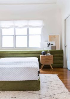 a bed sitting under a window next to a green couch in a room with hardwood floors