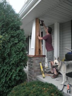 a man standing on the front porch with his dog next to him and working on something