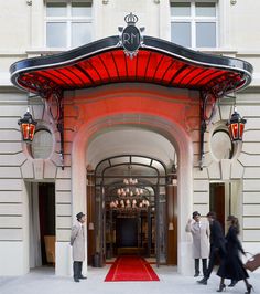 two men are standing in front of the entrance to an elegant building with red carpet