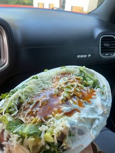 a plate filled with lots of food sitting on top of a car dash board next to a steering wheel