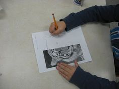 a person sitting at a table with a pencil in their hand and drawing a picture