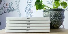 a stack of four books sitting on top of a table next to a potted plant