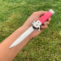 a person holding a pink and white knife in their hand on the grass with one blade missing