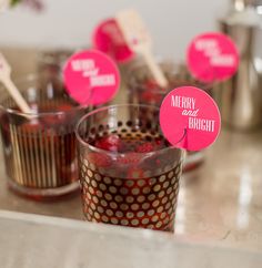 cupcakes with pink paper tags on them sitting on a counter next to cups