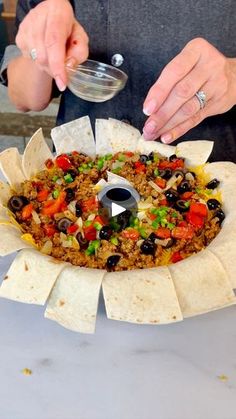 a person preparing food on top of a white plate with tortilla wrappers