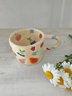 two daisies sitting next to a ceramic cup on a table with white flowers in the foreground