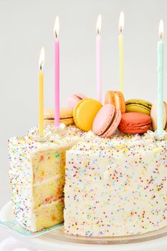 a birthday cake with white frosting and colorful sprinkles has five lit candles on it