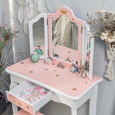 a pink and white dressing table with a mirror, stools and flowers in the corner