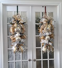 two christmas wreaths hanging on the front doors of a house, decorated with gold and silver ribbons