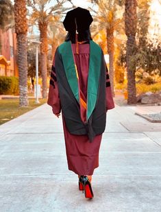 a woman in a graduation gown walking down the street wearing high heeled red shoes