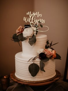 a white wedding cake with flowers and greenery on top that says the mcknesses